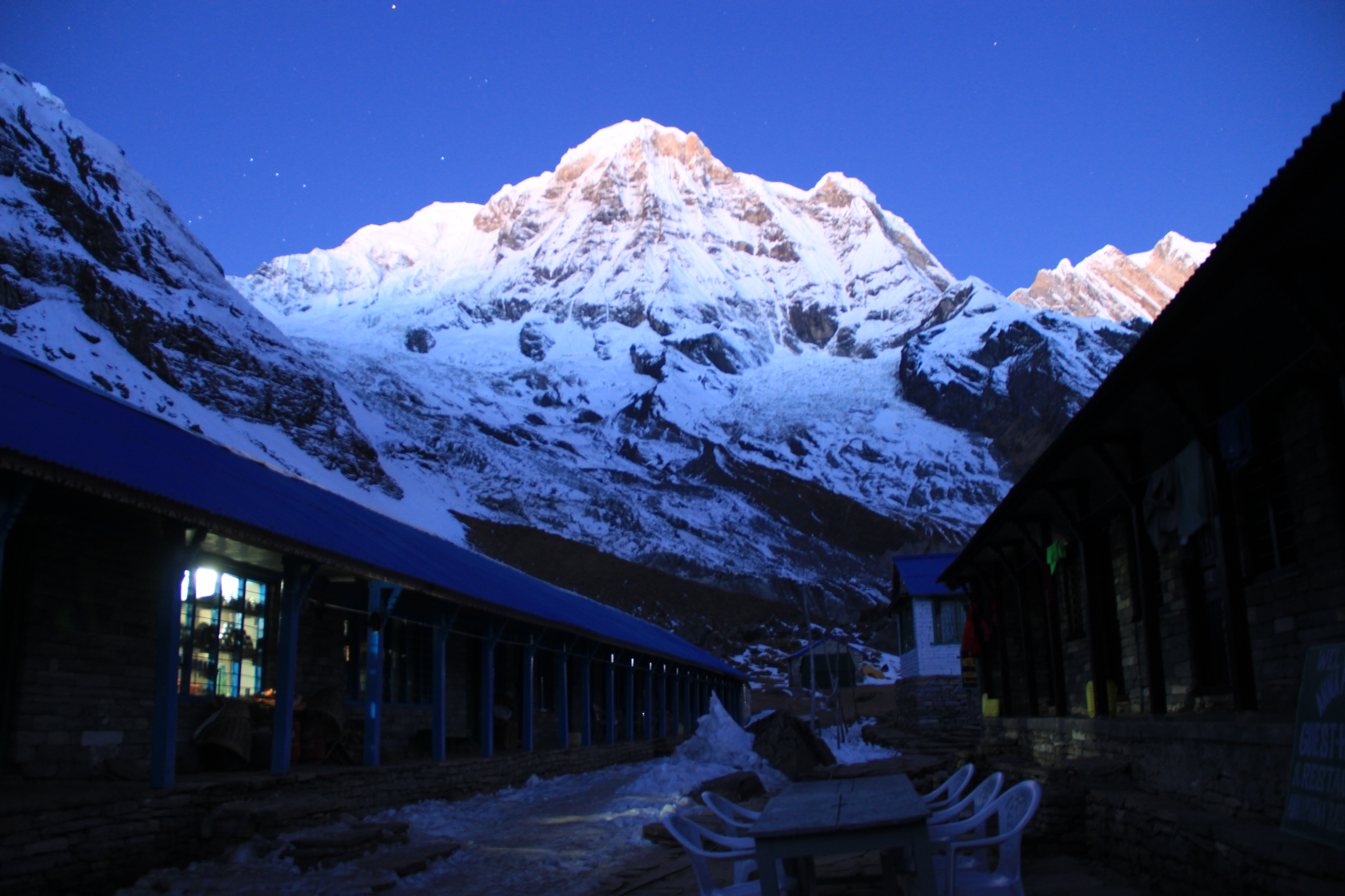 Breathtaking panoramic view of the snow-covered Annapurna sanctuary mountain range under a clear blue sky, as seen from the high-altitude Annapurna Base Camp trekking site.