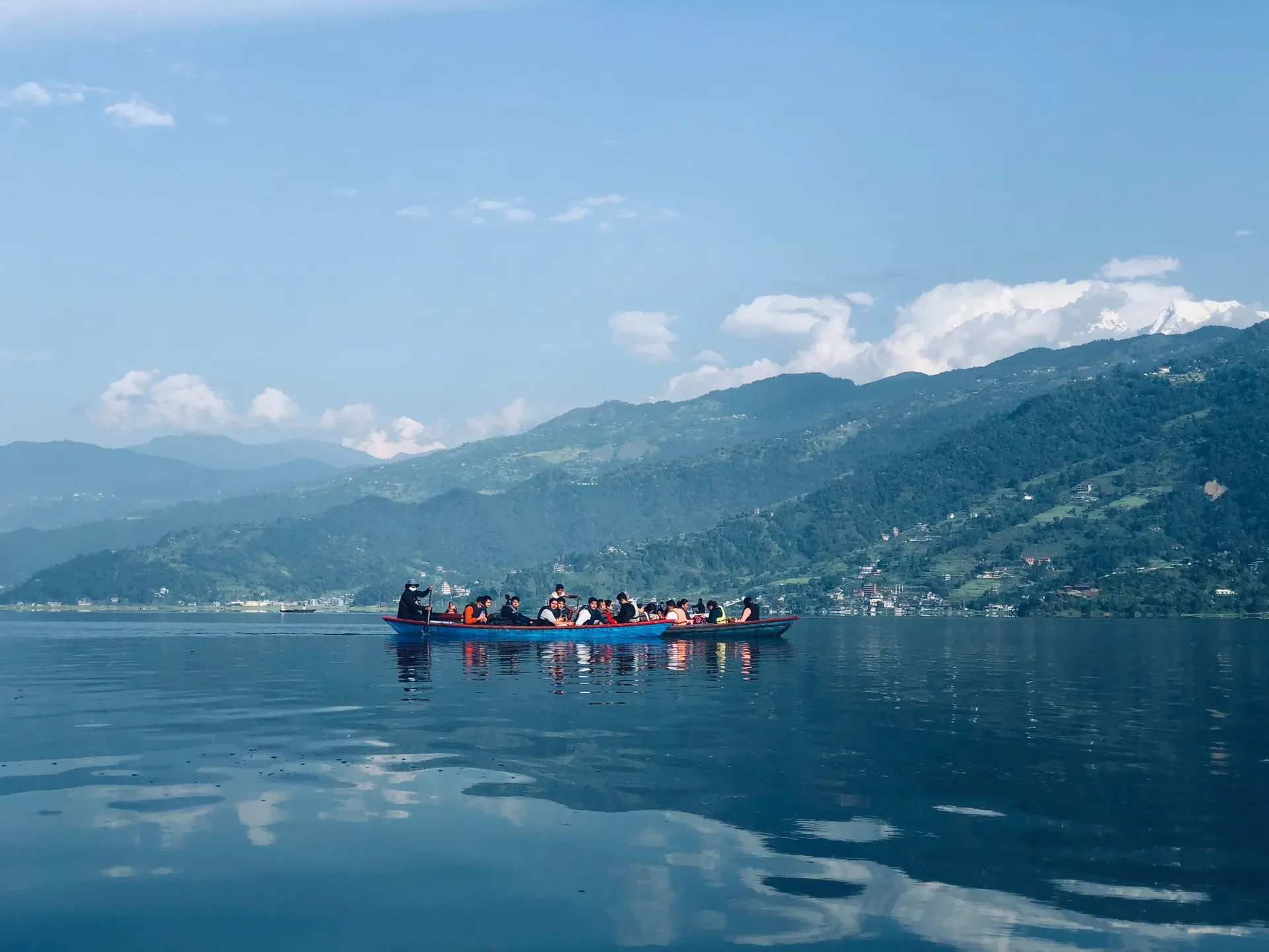 Tourists riding in colorful wooden boats on the calm, reflective waters of Phewa Lake in Pokhara.