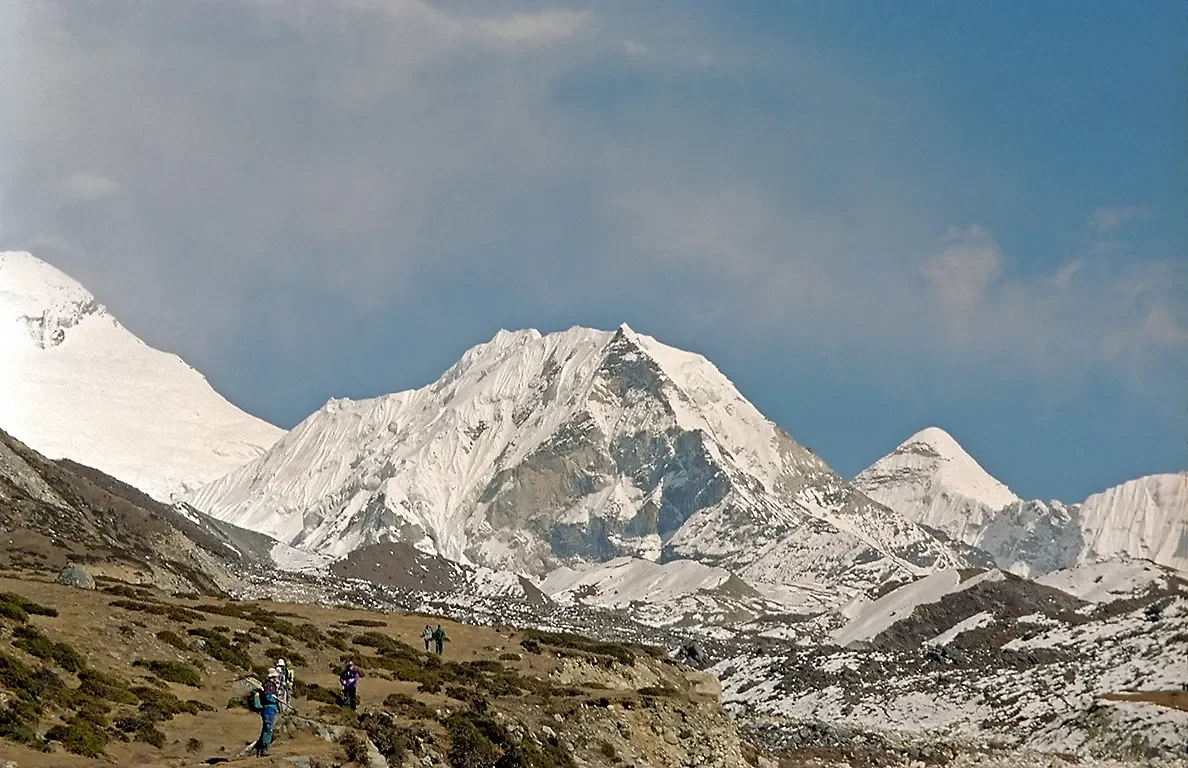 Hikers trekking on a mountain trail with snow-covered Himalayan peaks in the background
