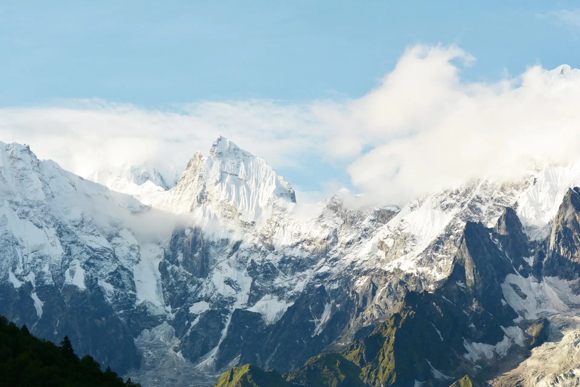 High-altitude view of the rugged, snow-covered peak of Mount Manaslu partially obscured by moving white clouds under a blue sky