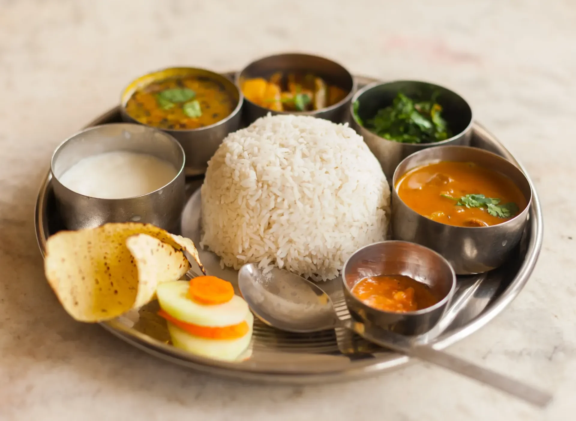 A traditional Nepalese Dal Bhat platter with steamed rice, lentil soup, vegetable curry, saag, pickle, and yogurt.