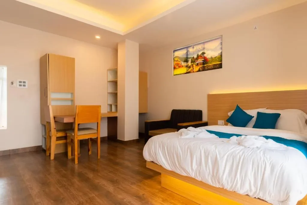 Modern studio apartment rental in Pokhara featuring a king bed with blue pillows, wooden flooring, and a small workspace desk