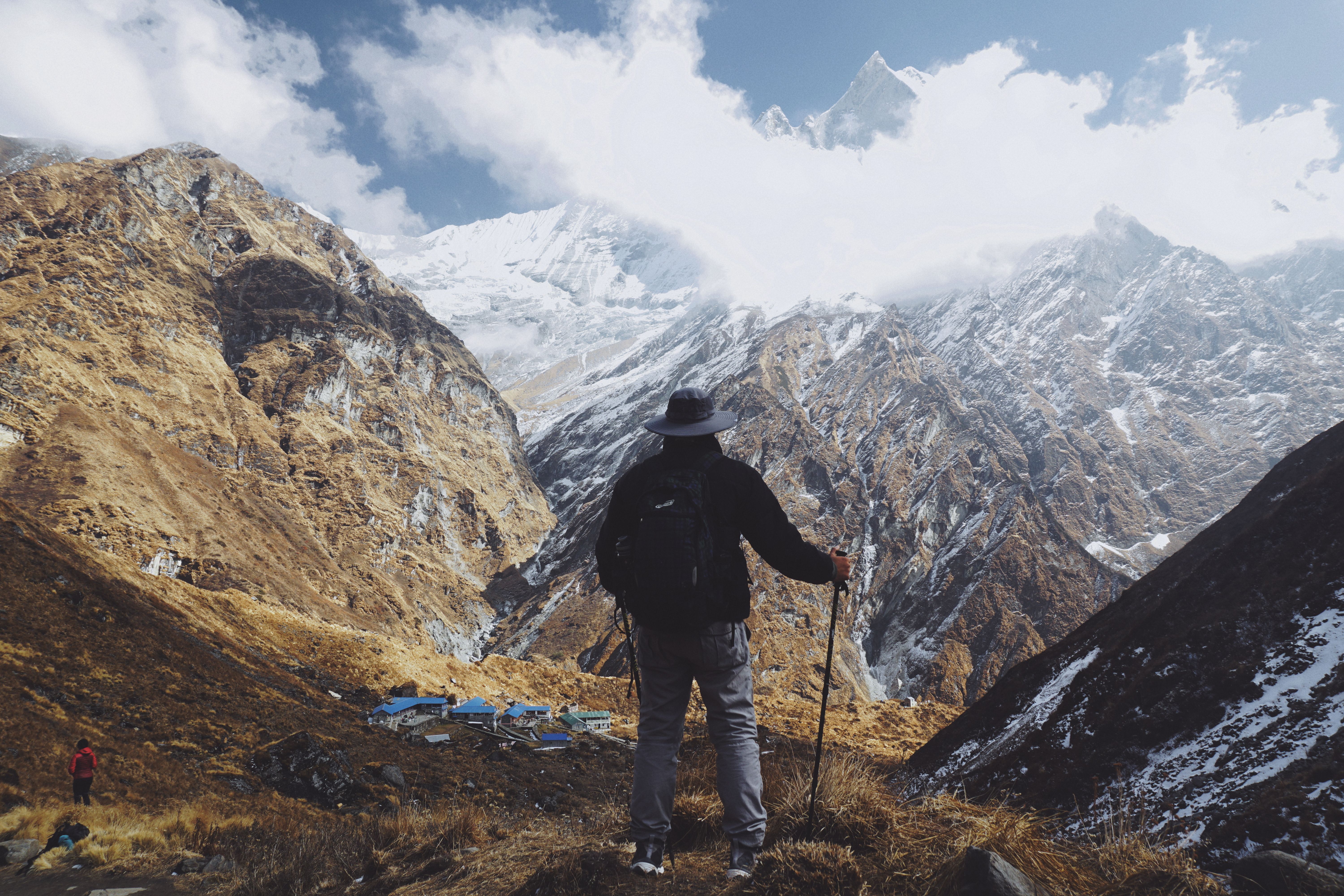 A solo hiker with a backpack standing on a ridge and overlooking a vast panoramic mountain valley view.