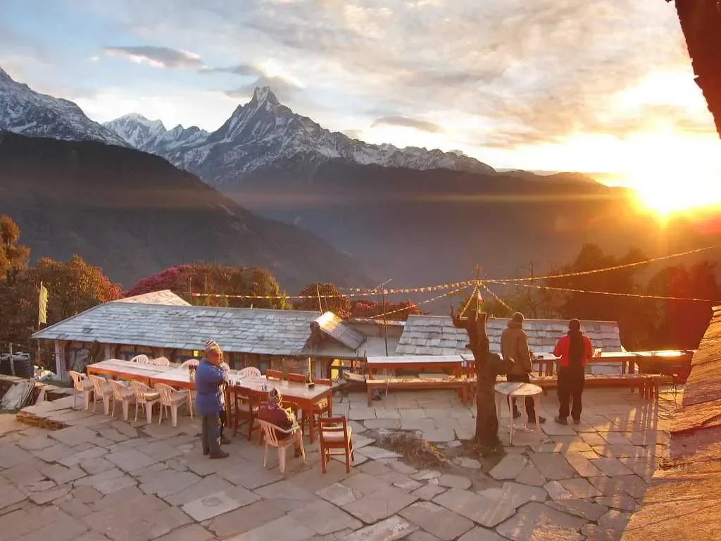 Trekkers gathered on a stone patio watching a golden sunrise hit Mount Machapuchare and the Annapurna mountains