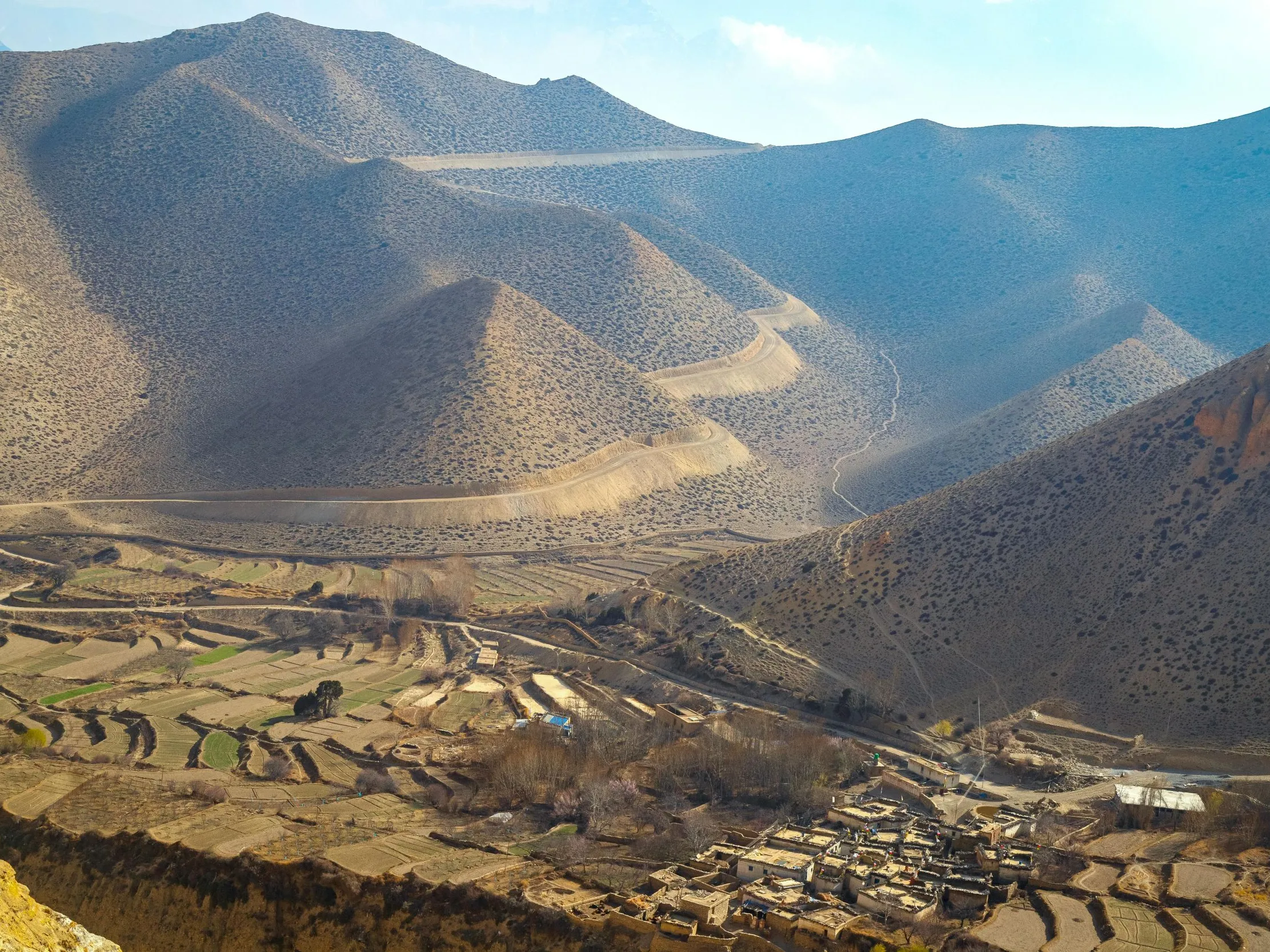 High-angle view of a remote mountain village in a dry, barren valley with winding roads in Upper Mustang.