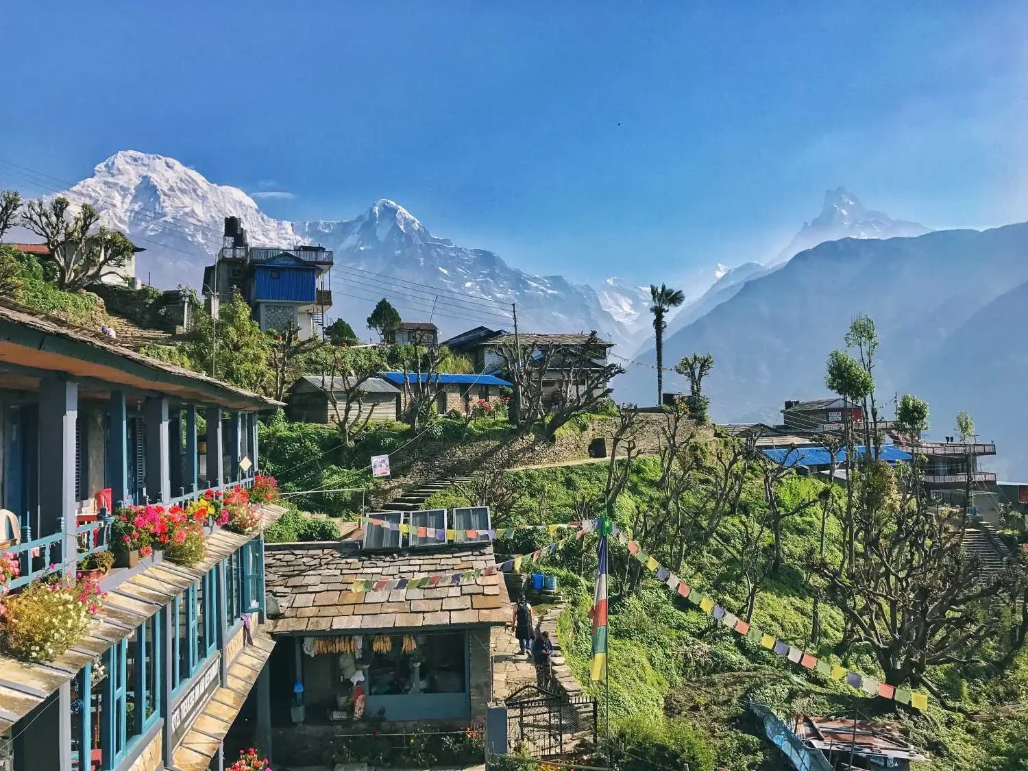 erraced hillside village of Ghandruk with traditional stone guest houses, colorful prayer flags, and towering Himalayan peaks in the background